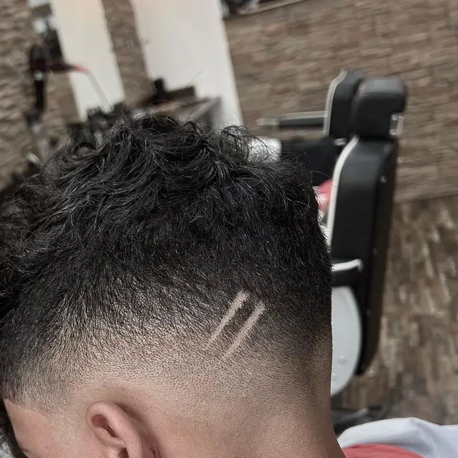 Lockiges Deckhaar mit hohem Skin Fade und zwei rasierten Linien an der Schl&auml;fe